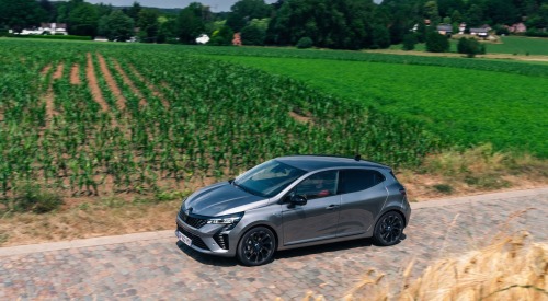 A used renault Clio driving on a cobbled road surrounded by fields of crops.