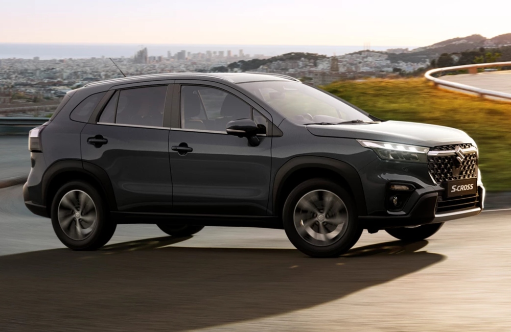 Angled side shot of a new Suzuki S-Cross driving up a windy countryside road at speed.