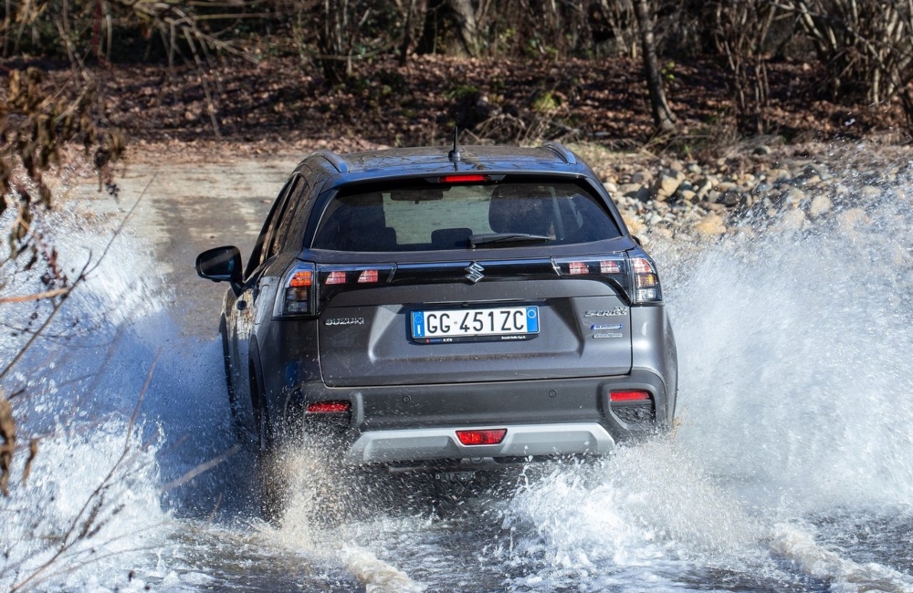 Rear shot of a new Suzuki S-Cross driving through a large puddle, spraying water everywhere.