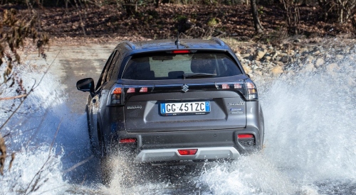 Rear shot of a new Suzuki S-Cross driving through a large puddle, spraying water everywhere.