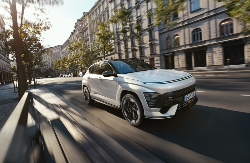 Angled front shot of a new Hyundai KONA Electric driving at speed down a city street.