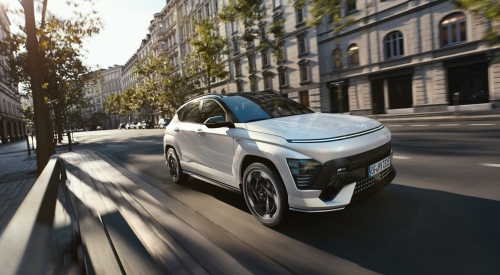 Angled front shot of a new Hyundai KONA Electric driving at speed down a city street.