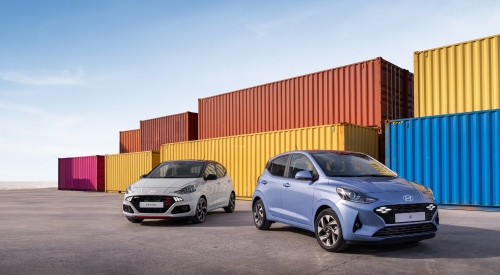 A new Hyundai i10 and i10 N Line parked next to each other in front of some shipping containers.