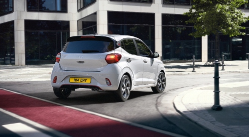 Rear shot of a white Hyundai i10 N Line driving at speed around a city street corner.