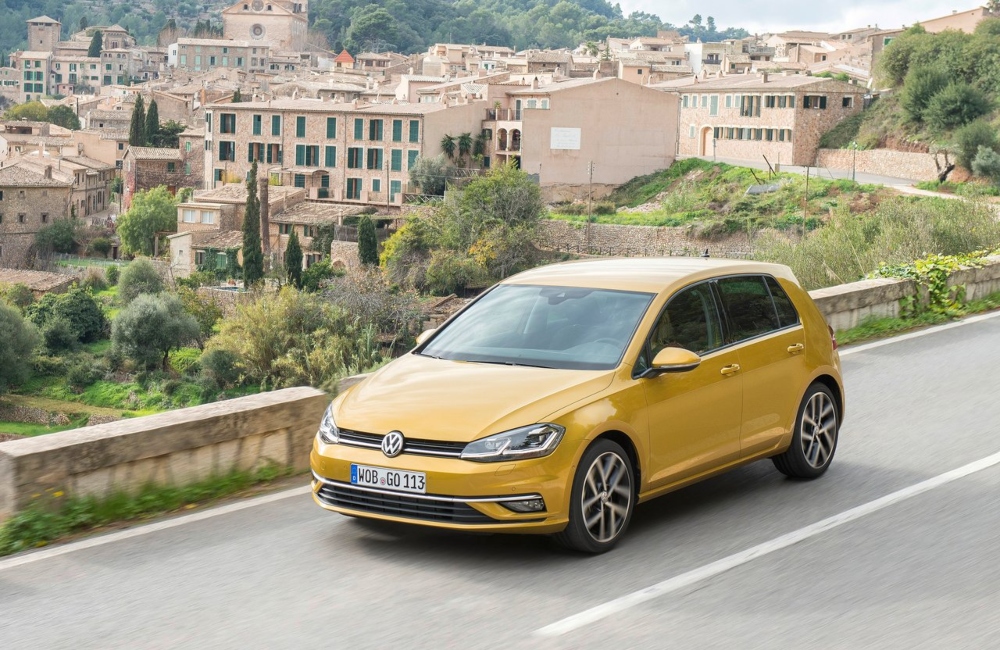 Golden yellow VW Golf driving down a country road at speed.