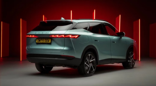 Angled rear shot of a new OMODA 7, showing off the unique rear design with a red backdrop.