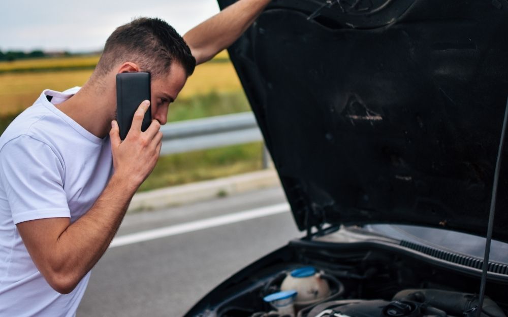 Person phoning for help beside a broken-down car