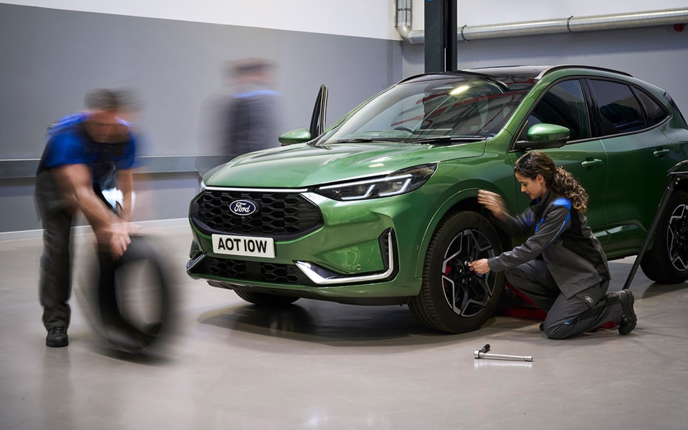 Technicians servicing a green Ford Kuga in a workshop.