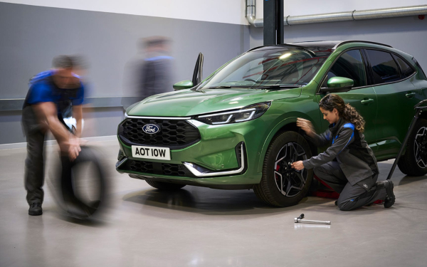 Technicians servicing a green Ford Kuga in a workshop.