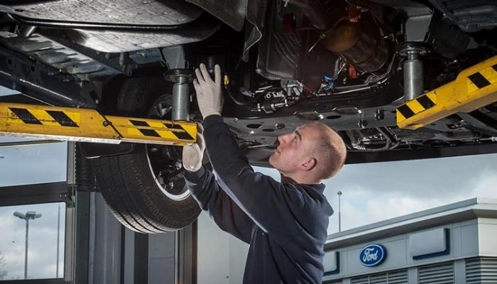ford repair technician inspecting the underside of a damaged car