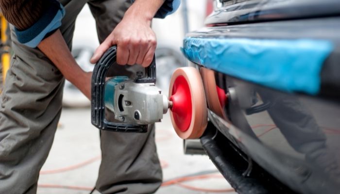 mechanic buffing a car bumper to repair scratch