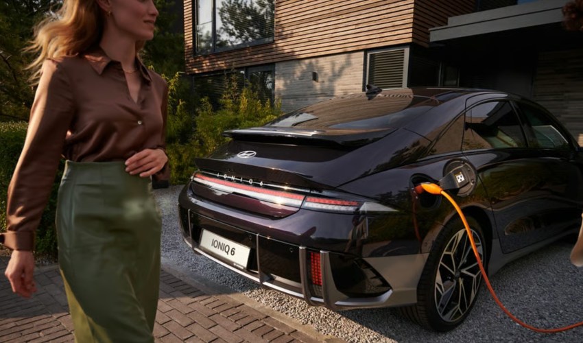 A woman walks past a Hyundai IONIQ 6 charging on a driveway; Charging an EV at home image