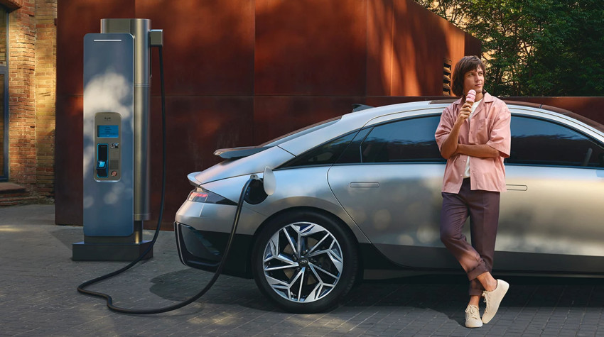 A woman leans by a charging Hyundai IONIQ 6; Cost of charging an EV intro image