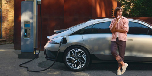 A woman leans by a charging Hyundai IONIQ 6; Cost of charging an EV intro image