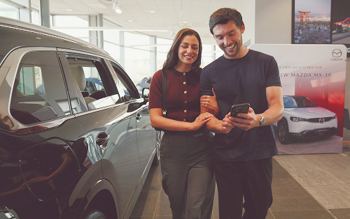 A couple look at a phone in front of a white car; bad credit car finance specialists image.