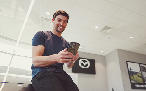 Man looks at phone happily in a car dealership; Bad credit car finance dealership image.