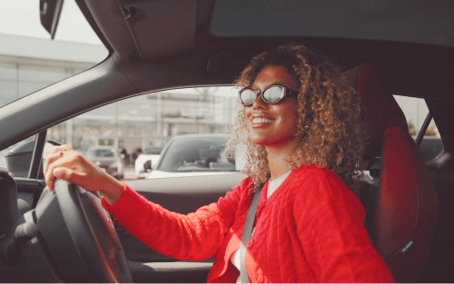 A woman happily drives her car away from a dealership; Applying for 0% interest car finance image