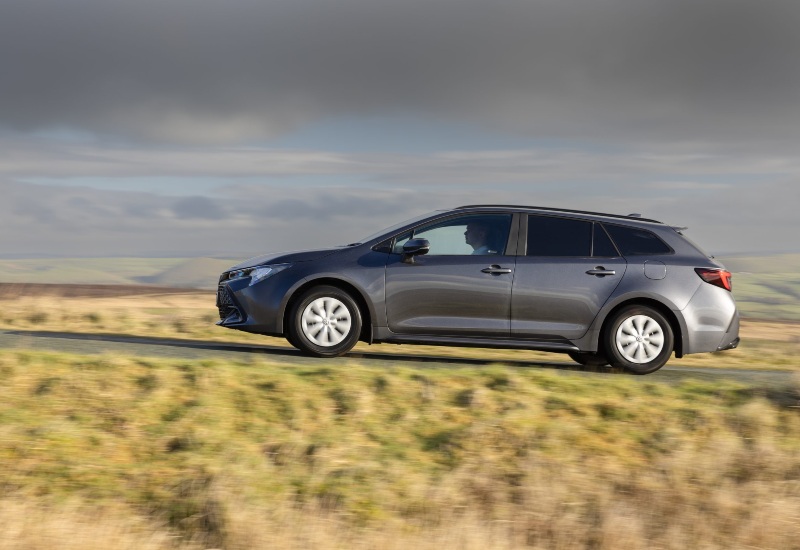 The new Toyota Corolla Commercial in grey, driving on a rural road with rolling hills in the background.