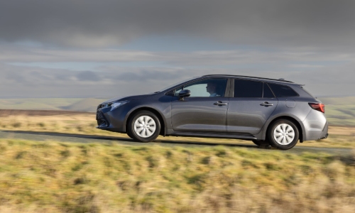 The new Toyota Corolla Commercial in grey, driving on a rural road with rolling hills in the background.