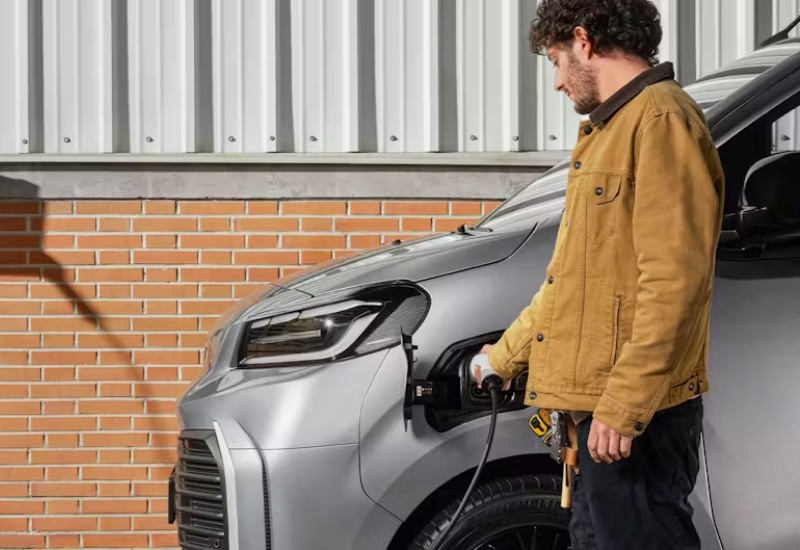 The new Toyota Proace Electric van in silver, charging at the front with a man plugging in the cable.