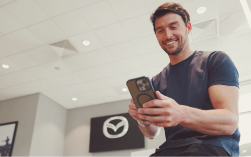 A man looks at a phone in a car dealership; How to improve your credit score image