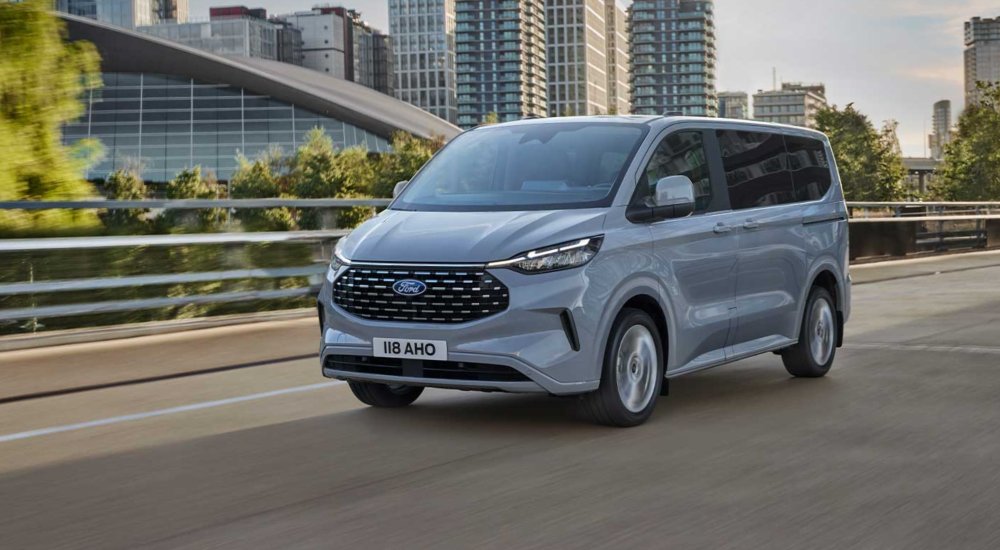 Ford Tourneo Custom driving through a modern city, shown from the front on an urban road.