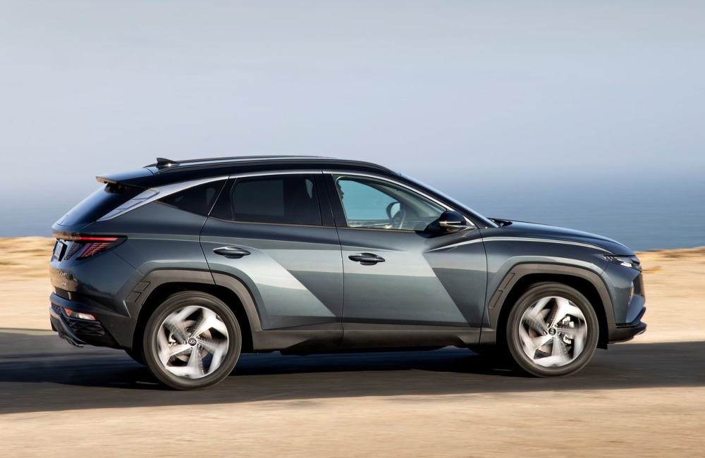 The side profile of a self-charging Hyundai TUCSON car, driving beside the beach