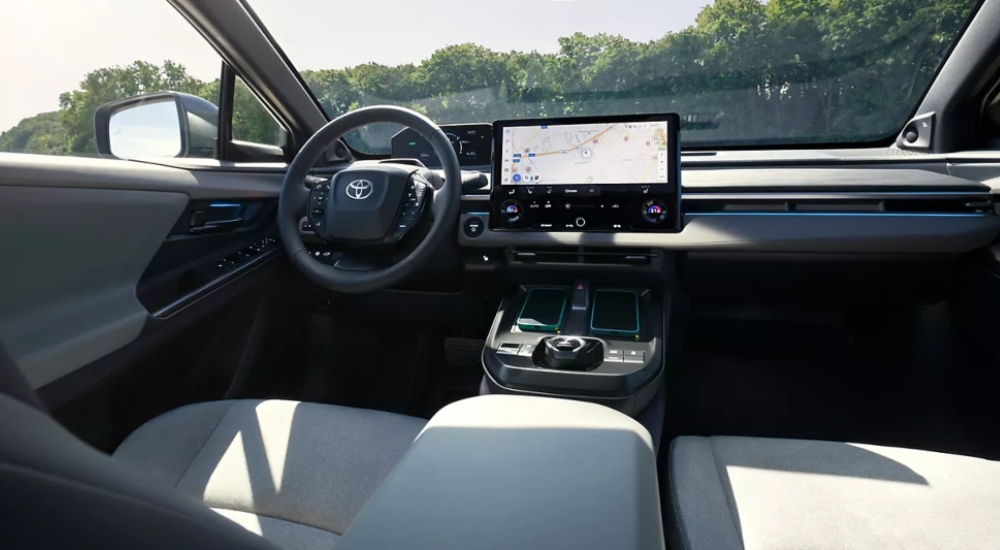 New Toyota C-HR+ interior showing 14-inch touchscreen display, steering wheel with integrated controls, and wireless charging pads.