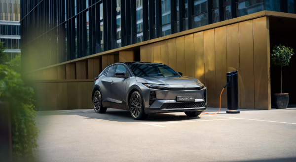 New Toyota C-HR+ electric car parked and plugged in for charging, showing front-side view and charging port.