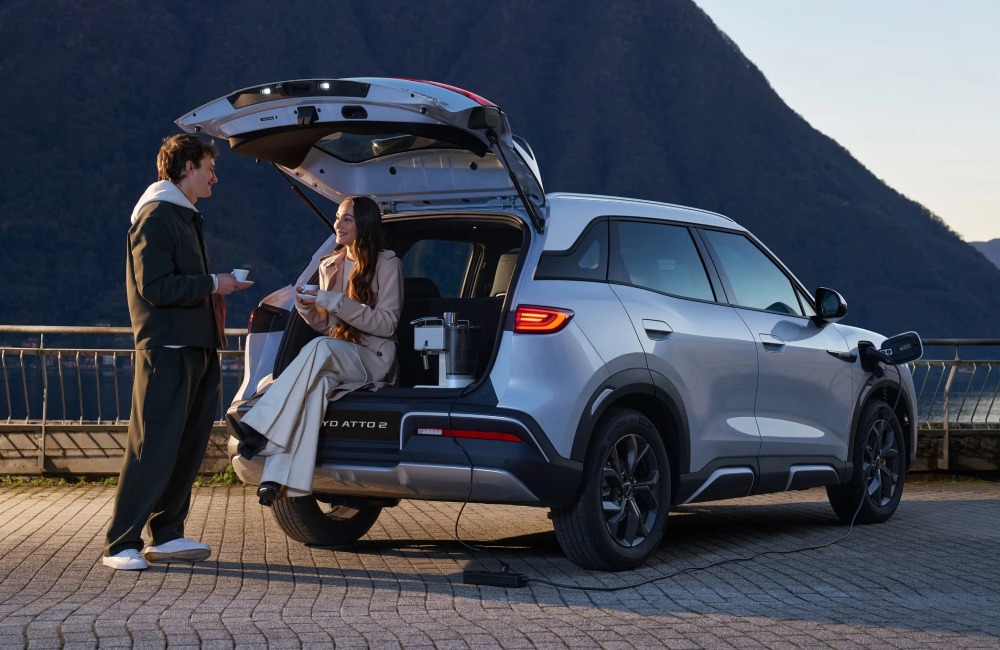 A happy couple sat on the edge of a new BYD ATTO 2 boot, making and drinking their own coffee