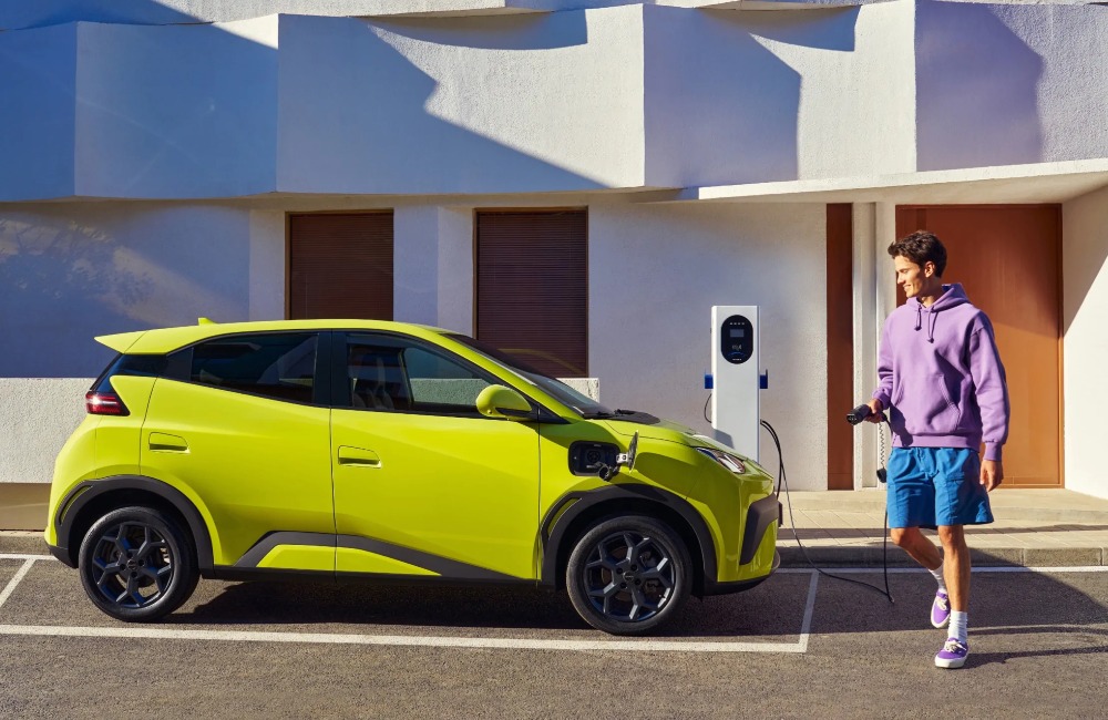 Person holding public charger in prep to plug in their used BYD car, which is parked within a bay next to the charger.