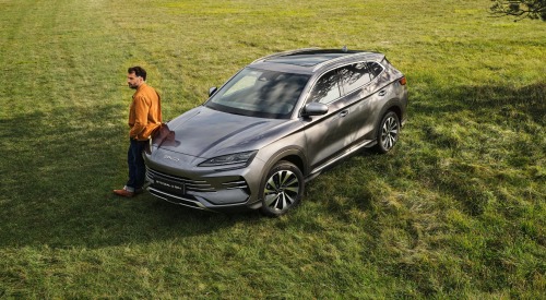 A top-angled shot of a person leaning on a used BYD car in a lush grassland.