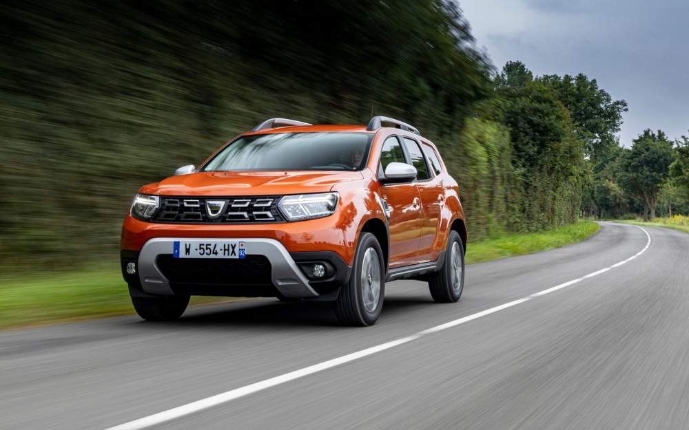 Front three-quarter view of an orange Dacia Duster driving on a rural road.