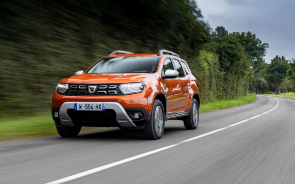 Front three-quarter view of an orange Dacia Duster driving on a rural road.