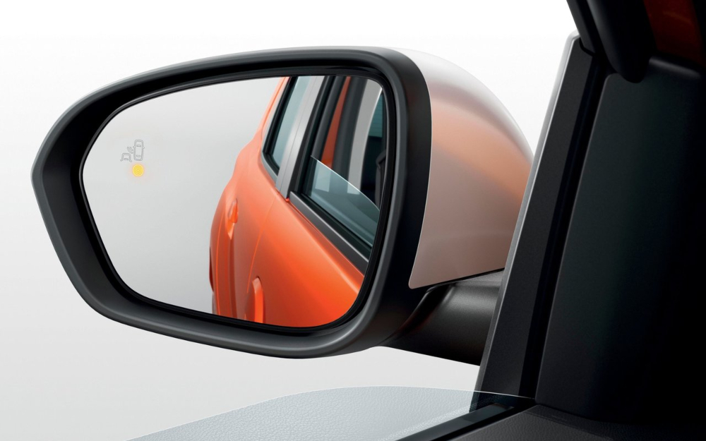Close-up of the side mirror on an orange Dacia Duster with Blind Spot Warning illuminated.