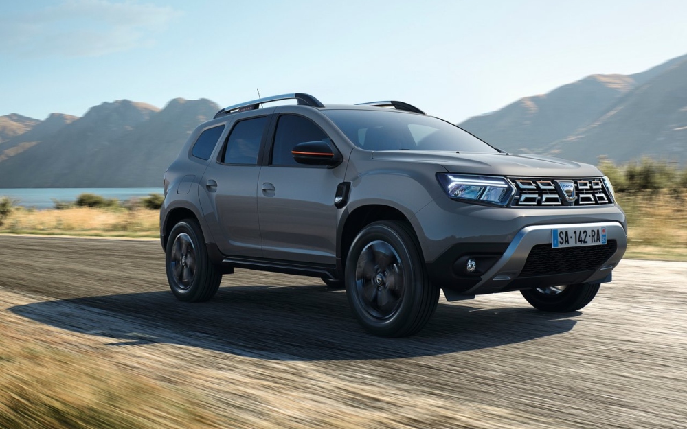 Front three-quarter view of a Dacia Duster driving through an open scenic landscape.