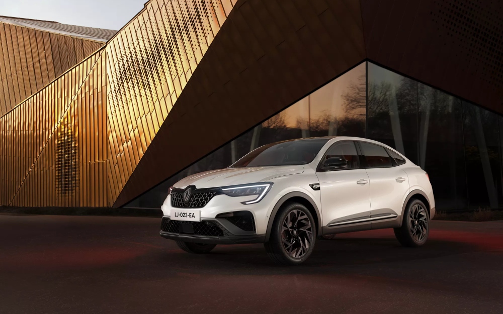 Front three-quarter view of a white Renault Arkana parked outside a modern building.
