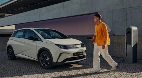 A person holding an electric car charger, walking towards a parked BYD DOLPHIN: Lease BYD