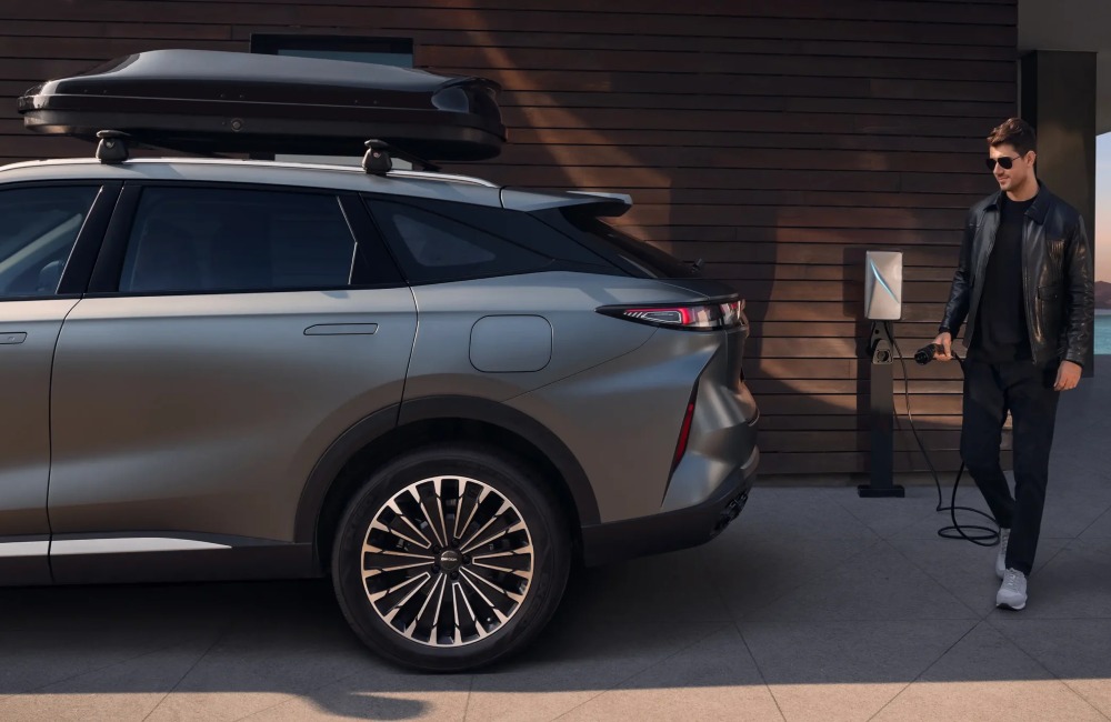 Back side of an OMODA 9, with a person walking up holding a charger in prep to charge the internal battery.