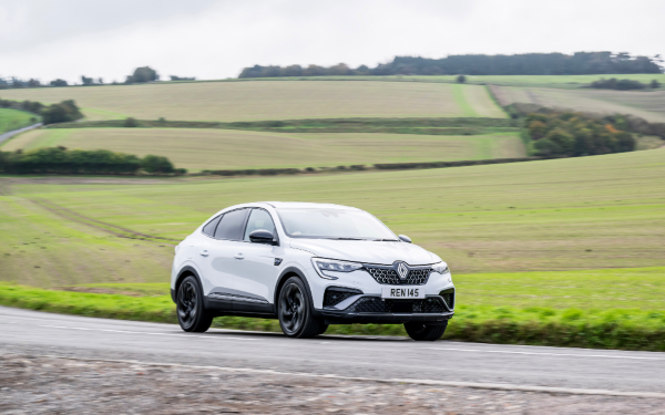 Used Renault Arkana E-Tech Renault Arkana E-Tech in white, driving on a country road with fields in the background.