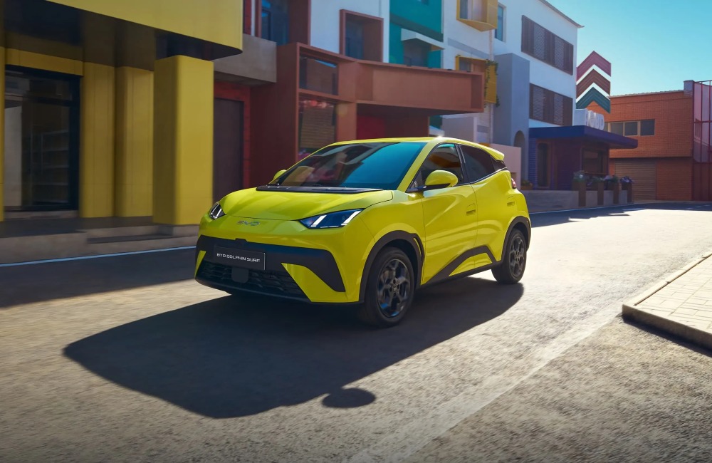 A vibrant yellow coloured BYD DOLPHIN SURF cruising down a futuristic city scape