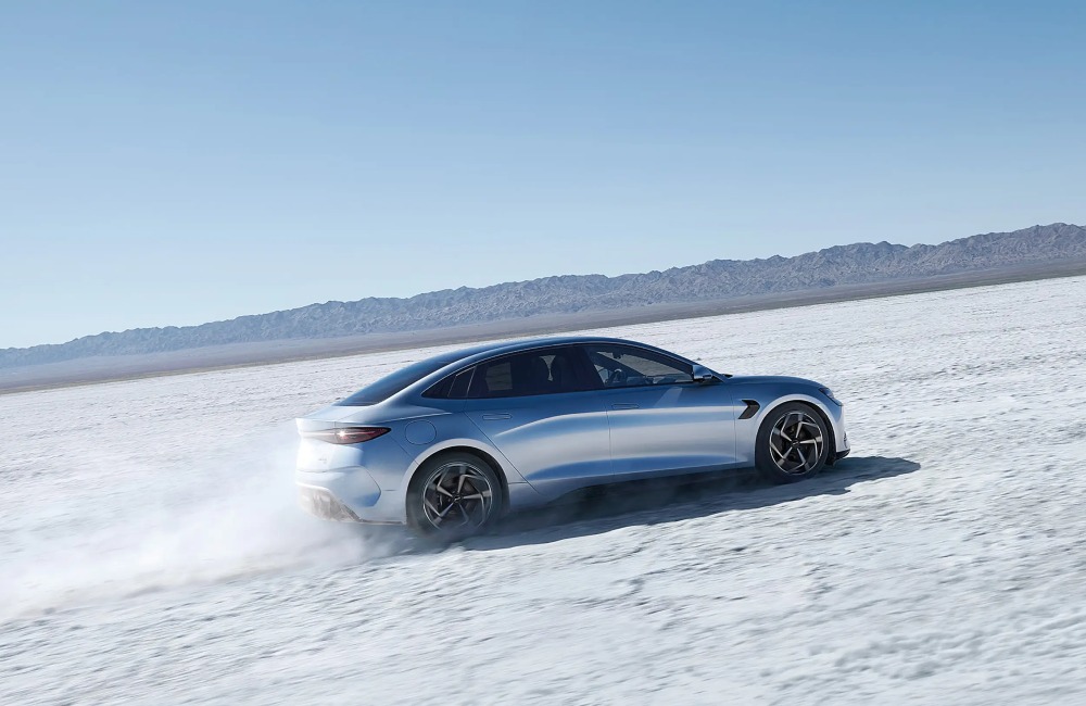 A BYD SEAL going at speed through a snowy landscape with a mountainous backdrop