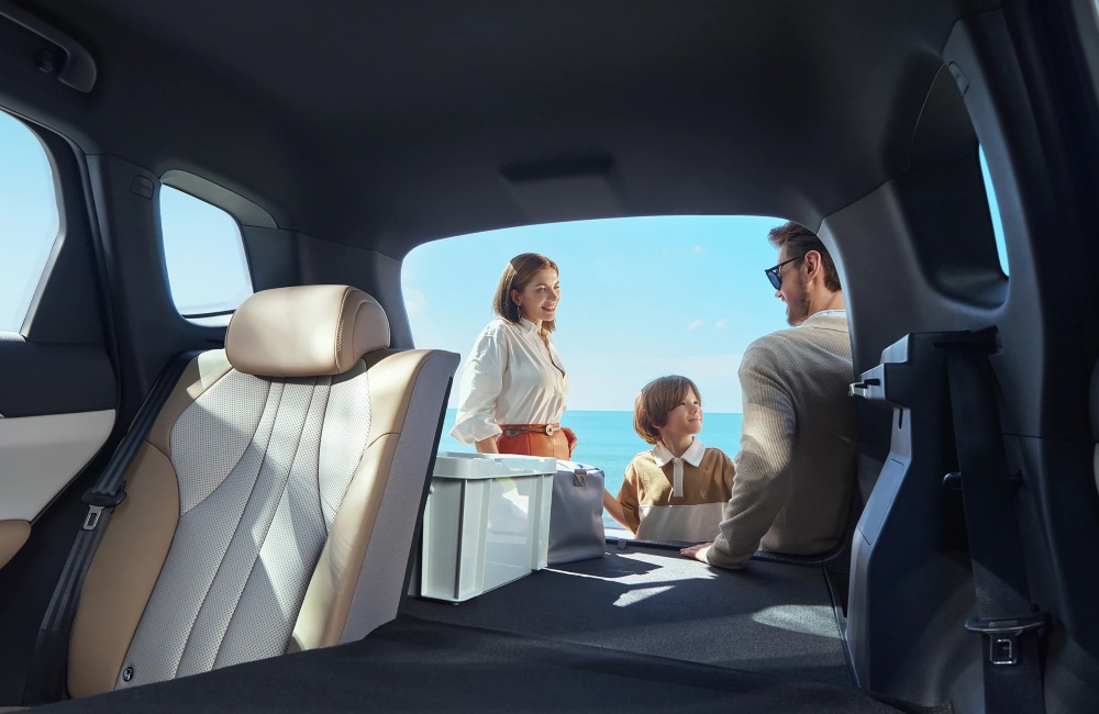 Interior view of the BYD SEALION 5 DM-i, showing a family loading up the boot with a seascape behind them, half the rear seats are folded to show off the expansive capabilities of the boot.