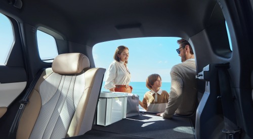 Interior view of the BYD SEALION 5 DM-i, showing a family loading up the boot with a seascape behind them, half the rear seats are folded to show off the expansive capabilities of the boot.