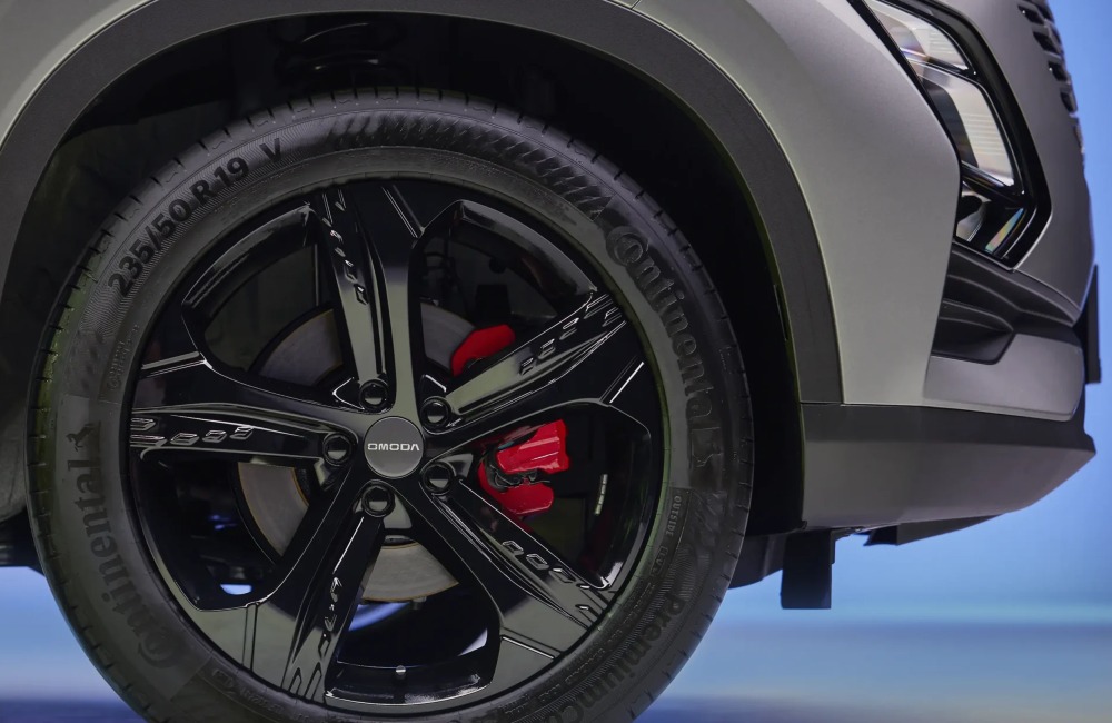 Close up view of an OMODA 5 black alloy wheel, boasting red brake caliper and OMODA branding.