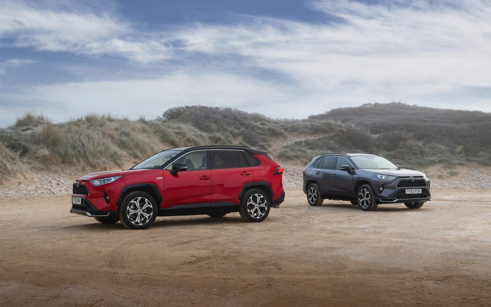 Used Toyota RAV4 PHEV cars in Scarlet Flare and Decuma Grey parked on sand.