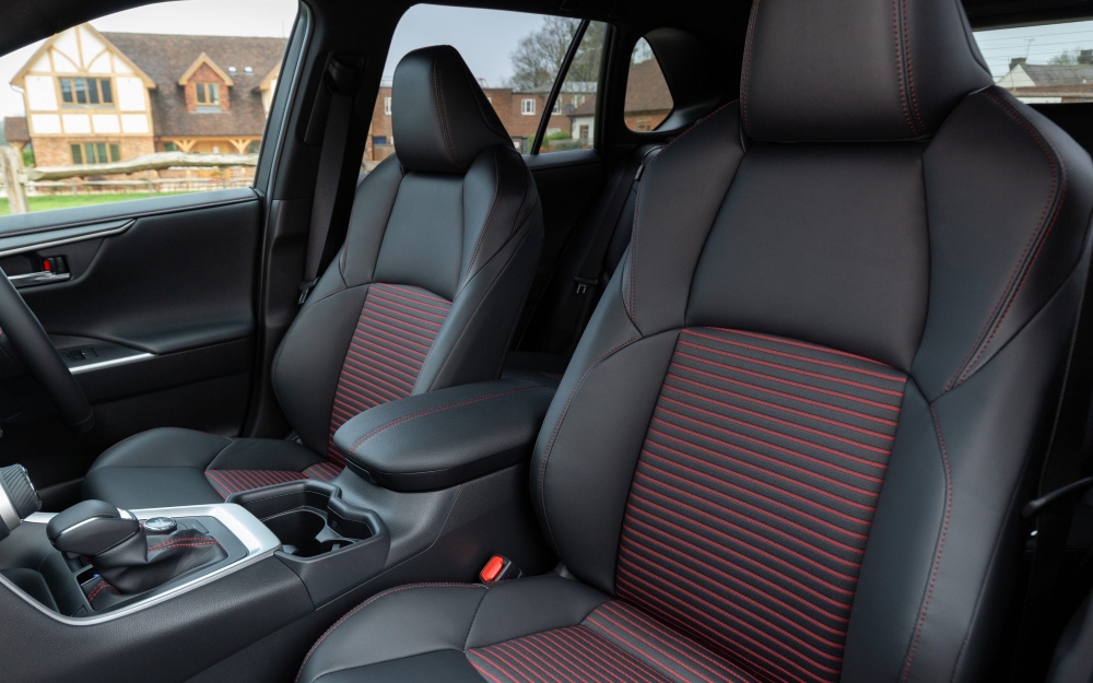 Used Toyota RAV4 PHEV interior with black leather front seats and red stitching.