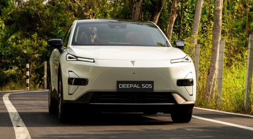 Front view of a Changan Deepal S05 driving down a country road surrounded by trees and brush. The car is white and showing off daytime running lights.