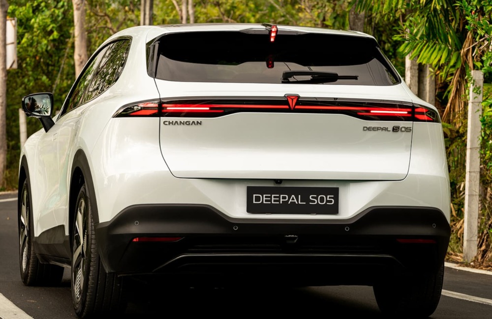 Rear view of a Changan Deepal S05 as it drives down a country road, surrounded by trees and shrubbery.