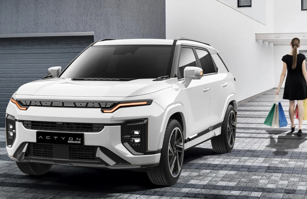 A person walking away from a KGM Actyon Hybrid, holding some shopping and going into their house.